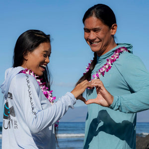 Man and woman wearing Humu Woody Bamboo Lightweight Hoodies in marine blue and light blue beside the ocean
