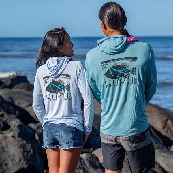 Man and woman wearing Humu Woody Bamboo Lightweight Hoodies with large back fish graphics by the ocean