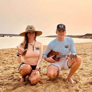 Man and woman wearing Humu Woody Bamboo Long-Sleeve Sun Shirts with a Classic Lifeguard Hat and Original Black Trucker Hat