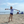 Load image into Gallery viewer, Child wearing the white Humu Juniors Classic Long-Sleeve Unisex Rash Guard while standing on the beach
