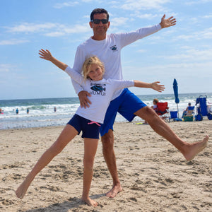 Child in a Humu Juniors Classic Long-Sleeve Rash Guard with their dad wearing a white Humu brand Men's Woody Long Sleeve Performance Sunshirt