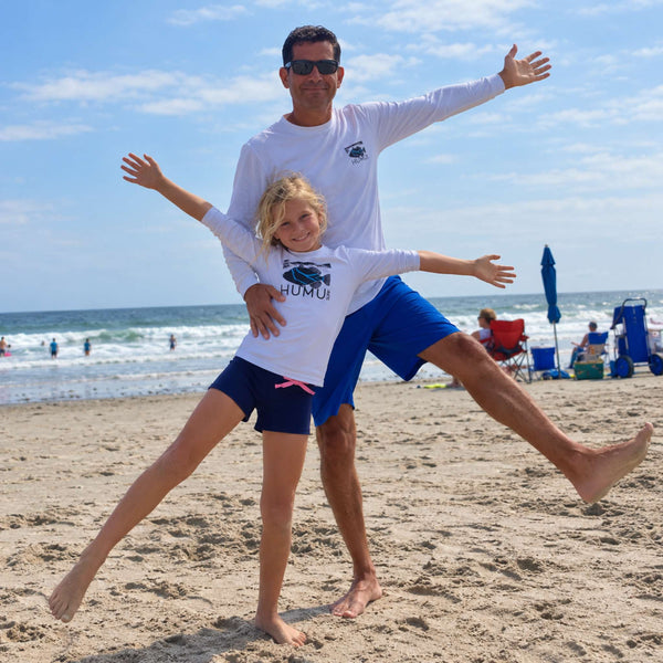 Child in a Humu Juniors Classic Long-Sleeve Rash Guard with their dad wearing a white Humu brand Men's Woody Long Sleeve Performance Sunshirt