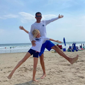 Child in a Humu Juniors Classic Long-Sleeve Rash Guard with their dad wearing a white Humu long-sleeve performance sun shirt on the beach
