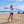 Load image into Gallery viewer, Child wearing the white Humu Juniors Classic Long-Sleeve Unisex Rash Guard while standing on the beach
