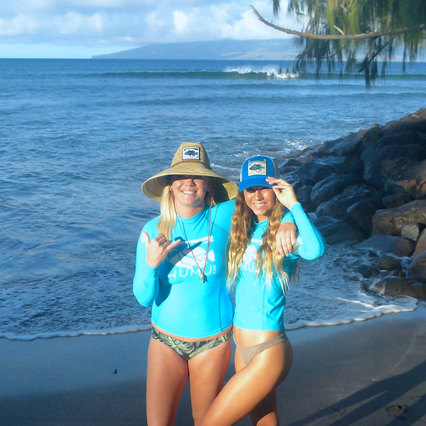 Two women wearing blue Humu Wahine Kore-Dry Long Sleeve Rashguards with a Classic Lifeguard Hat and Molokini Trucker Hat