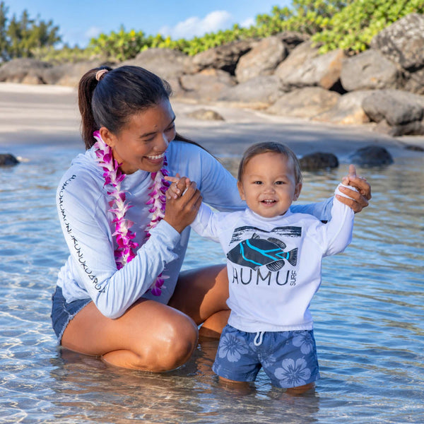 Woman wearing a Humu Women's Woody Bamboo Lightweight Hoodie holding hands with a toddler in a white Humu Juniors Classic Long Sleeve Rash Guard in shallow ocean water