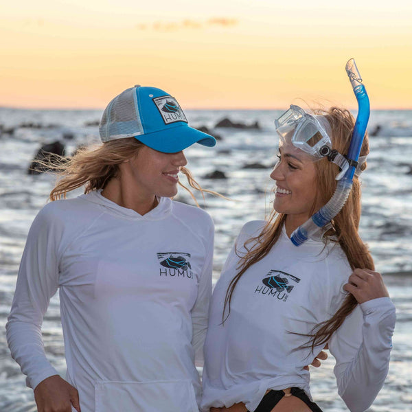 Two women wearing white Humu Women's Woody Long Sleeve Performance Hoodies by the ocean, one with snorkeling gear