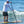 Load image into Gallery viewer, Man wearing the white Humu Men's Woody Long Sleeve Performance Hoody while stand-up paddleboarding on an ocean wave, showing the large Humu fish graphic on the back

