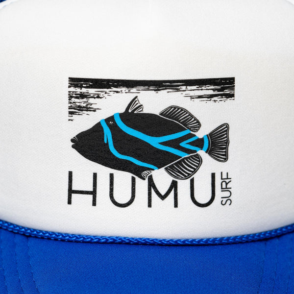 Close-up of the Humu Surf fish logo on the white front panel of the royal blue Original Trucker Hat
