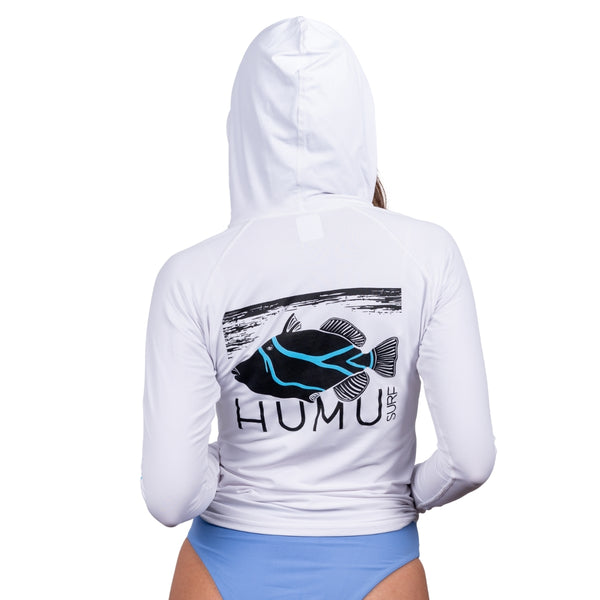 Rear view of a woman wearing the white Humu Woody Long Sleeve Performance Hoody with hood up and large black and turquoise Humu Surf fish graphic across the back