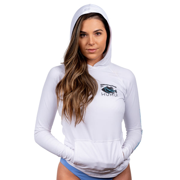 Woman wearing the white Humu Women's Woody Long Sleeve Performance Hoody with the hood up, showing the fish logo and front pouch pocket
